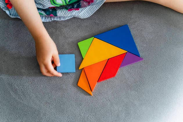Weltkindertag am 20. September Woman playing with multi colored tangram on sofa model released Symbolfoto property released DIGF16116