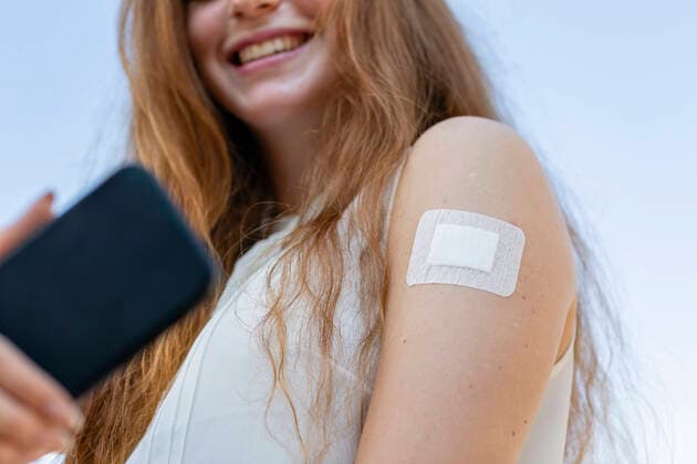 Smiling businesswoman with vaccine on arm taking selfie through smart phone during COVID-19 model released Symbolfoto EIF01486