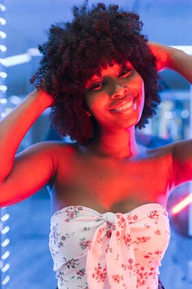 Young Afro woman with hand in hair near neon lights model released Symbolfoto JRVF01126