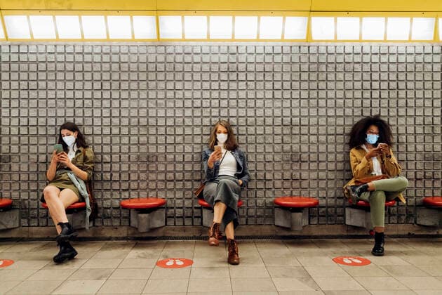 Friends with protective face mask using mobile phone while sitting at social distance in subway model released Symbolfoto MEUF03526