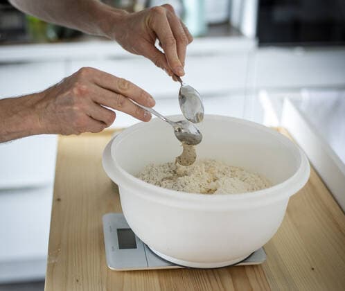 Symbolfoto zum Thema Brotbacken. Sauerteig wird zum. Wiegen mit zwei Loeffeln zum Mehl hinzu gegeben. Berlin, 02.02.2021. Berlin Deutschland *** Symbol photo on the subject of bread baking Sourdough is added to the flour for weighing with two laffs Berlin, 02 02 2021 Berlin Germany Copyright: xJaninexSchmitz photothek.dex