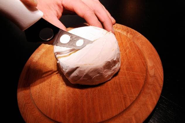 cutting a camembert in the middle with a cheese knife on a round wooden board camembert, a creamy soft cheese