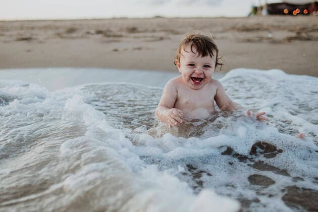 Male toddler laughing while sitting in water at beach during sunset model released Symbolfoto GMLF00754