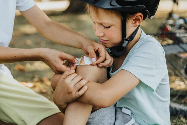 Boy putting bandage on younger brother knee sitting in public park model released Symbolfoto MFF06376