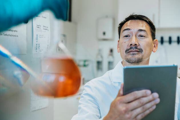 Scientist looking at liquid flask while using digital tablet at laboratory model released Symbolfoto property released MFF06480