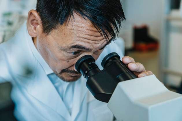 Male scientist looking though microscope while man standing in background at laboratory model released Symbolfoto property released MFF06499