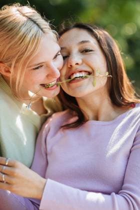 IMAGO Creative: Sommer, Sommertage im Garten Delighted teen sisters with grass twig in teeth embracing and having fun on sunny day in garden, Model released CamilleGirard_TwoSistersOnACouch_13.jpg Copyright: xCamillexGirardx MR