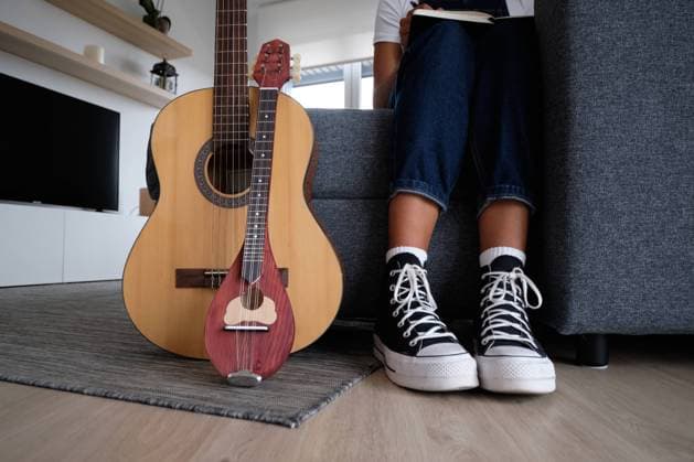 Crop unrecognizable African American female musician sitting on sofa near acoustic guitar and mandolin Pempki_MusicAndWorkAtHome_11.jpg Copyright: xPempkix Model Released