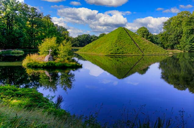 Seepyramide im Branitzer Park DEU Brandenburg Cottbus Â Die Seepyramide (Tumulus) , ist das Wahrzeichens des Branitzer Parks. Der von Fürst Herrman von Pückler-Muskau (1785-1871) geschaffene 530 Hektar große Landschaftspark im englischen Stil gehört zu den besonderen Anziehungspunkten von Cottbus. Er ist ein Gartenkunstwerk von internationaler Bedeutung. Mit der im Herbst rot leuchtenden Seepyramide (Bauzeit 1856-57) setzte sich der extravagante Gartenfürst selbst ein Denkmal. Noch heute wird die Pyramide von den beiden originären Weinsorten Uferrebe und Jungfernrebe begrünt. Fürst Pückler wurde 1871 im Tumulus (der Seepyramide) beerdigt, 1884 wurde auch seine bereits 1854 verstorbene Frau und Lebensgefährtin, Lucie von Pückl