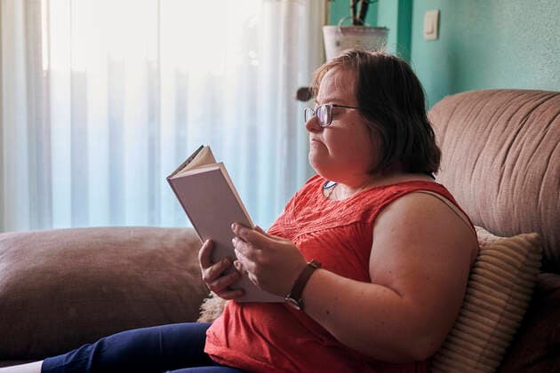 Down syndrome woman reads a book on the couch at home Villena, Valencian Community, Spain CR_CRBL210729-804263-01 ,model released, Symbolfoto