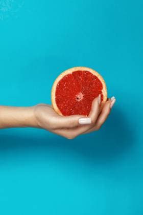 Crop anonymous female with manicure holding half of fresh juicy grapefruit with red pulp against blue background, Model released AdrianSava_Hands_2.jpg Copyright: xAdrianxSavax MR