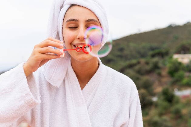 Creative Highlights Symbolbilder Young woman in white bathrobe and towel blowing soap bubbles during spa session on balcony DavidMunoz_LuciaRoom_38.jpg Copyright: xDavidxMunozx Model Released