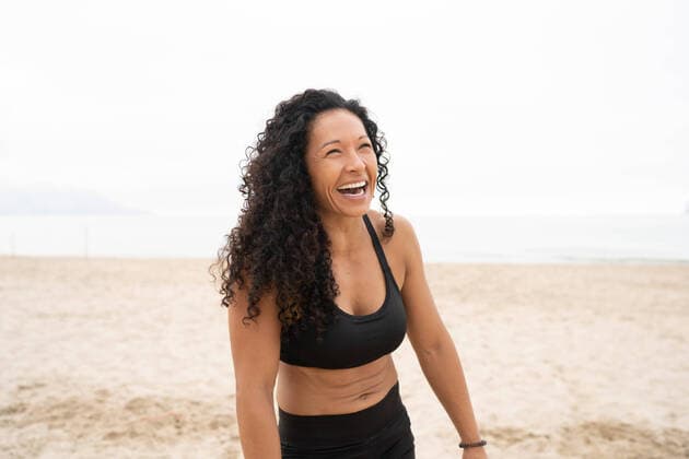 Creative Highlights Symbolbilder Positive Asian female athlete with curly hair laughing on sandy seashore in summer, Model released OscarDeDios_FitnessWithDeli_25.jpg Copyright: xOscarxDexDiosx MR