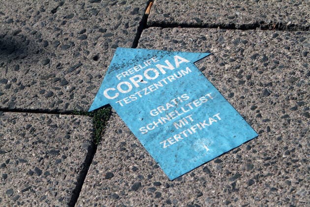 Sticker with directional arrow and inscription Freelife Corona Testzentrum free quick test with certificate sticks on a sidewalk in downtown Munich, Bavaria, Germany