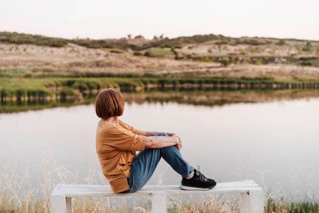 Senior woman looking at mountains while sitting on bench near lake model released Symbolfoto EBBF04427