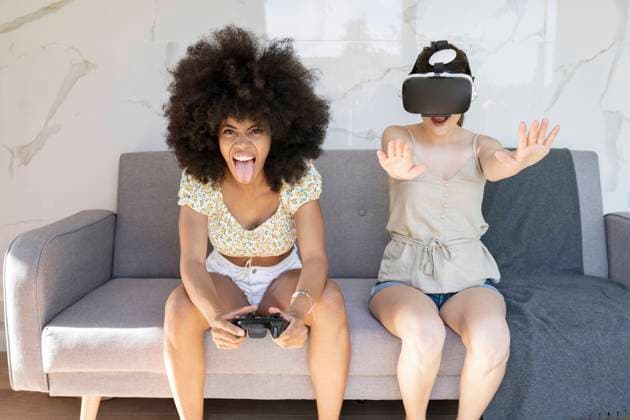 Afro woman sticking out tongue while female friend wearing virtual reality headset at home model released Symbolfoto property released JCCMF03236