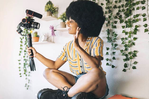 Young Afro influencer waving while vlogging through camera at home model released Symbolfoto property released JCCMF03323