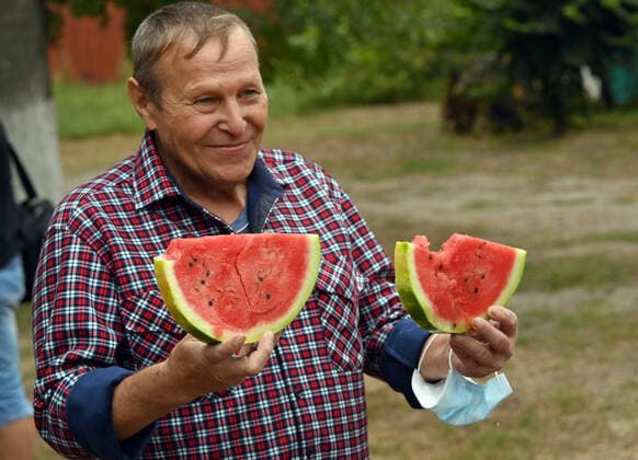 SIEVIERODONETSK, UKRAINE - AUGUST 24, 2021 - A man in a checked shirt holds two slices of a watermelon during the Bashtan Fest, a watermelon festival in Sievierodonetsk, Luhansk Region, eastern Ukraine. Watermelon festival in Sievierodonetsk  Copyright: xOleksiixKovalovx