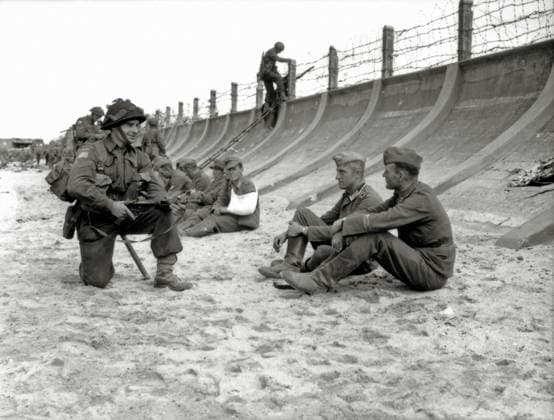Corporal Victor Deblois from the 3rd Canadian Infantry Division crouching weapon in hand before two German prisoners sitting at the foot of the concrete dam at Juno Beach. June 6, 1944. Other prisoners are sitting along the concrete dam in the background near Widerstandsnest (Wn) 28. The German garrison of Berni?res-sur-Mer belonged to the 5. Kompanie II Grenadier Regiment 736 of the 716 Infantrie Division. Photo: Lieutenant Frank L. Dubervill. Berni?res-sur-Mer, Normandy, France. ! ACHTUNG: AUFNAHMEDATUM GESCHÄTZT! *** Corporal Victor Deblois von der 3. kanadischen Infanteriedivision hockt mit der Waffe in der Hand vor zwei deutschen Gefangenen, die am Fuße des Betondamms am Juno Beach sitzen 6. Juni 1944 Weitere Gefangene sitzen entlan