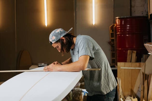 Side view of male shaper using measure tool while working with surfboard in workshop, Model released CarlosRodelas_SurfShapper_7.jpg Copyright: xCarlosxRodelasx MR