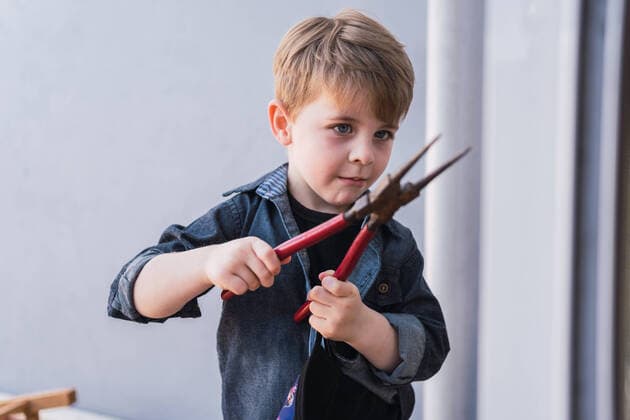 IMAGO Creative: Jahreszeit Winter, Fantasievoll drinnen spielen Attentive child with blue eyes in denim shirt looking at pliers against wall in daylight, Model released ReneStevens_PlayingWithWood_2.jpg Copyright: xx MR