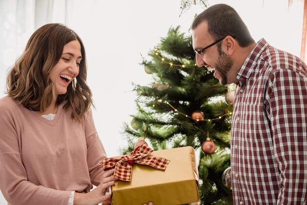 Cheerful adult female passing present box to astonished male beloved while celebrating New Year holiday in house, Model released, Property released SiAndSi_Christmas_64.jpg Copyright: xSixAndxSix MR