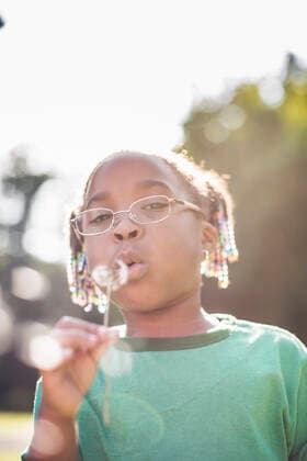 IMAGO Creative: Klimawandel - Umwelterziehung Portrait of girl blowing dandelion clock in parkland eco camp, 01.09.2014, Copyright: xChadxSpringerx, model released, wearing,learning,holding,camping,looking at camera,looking up,green color,copy space,differential focus,front view,head and shoulders,portrait,childhood,responsibility,harmony,innocence,well being,happiness,hope,nature,child,african american ethnicity,female,girl,only one girl,one person,outdoors,rural,summer,day,casual clothing,eyeglasses,t-shirt,education,environmental issue,environmental conservation,blowing,lifestyle,leisure,5 to 6 years,only female,dandelion clock,dandelion seed,parkland,September 2014 Release,Blowing,Thinking,Learning,Holding,Looking Up,Camping,African Descent,African American Ethnicity,Child,Eleme Ref:IS09AK90X