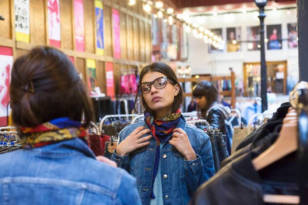 Over shoulder mirror image of young female shopper trying on scarf in market hall, 10.05.2017, Copyright: xAnoukxdexMaarx, model released, buying,trying on,wearing,shopping,head and shoulders,reflection,consumerism,decision,feminine,real people,retro,aspiration,bonding,sharing,togetherness,friendship,wall mirror,20 to 24 years,caucasian ethnicity,young woman,only young women,shopper,two people,people in the background,indoors,clothes shop,clothing,casual clothing,eyeglasses,fashion,scarf,denim jacket,lifestyle,leisure,youth culture,enjoyment,only female,Art Director s Choice,over the shoulder view,market hall,mirror image,second hand,best friends,vintage shop,looking in mirror,May 2017 Release,Buying,Shopping,Getting Dressed,Trying On,Ca Ref:IS09B5TK5