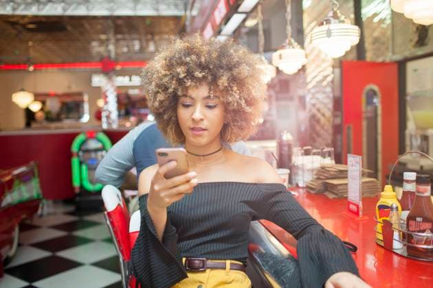Young woman sitting in diner, looking at smartphone, 15.09.2017, Copyright: xFranekxStrzeszewskix, model released, , property released, wearing,holding,looking,using,waiting,city living,concentration,connections,cool,focus concept,real people,individuality,boredom,young adult,20 to 24 years,female,woman,young woman,only one young woman,one person,diner,fast food restaurant,indoors,united kingdom,england,london,day,casual clothing,communication,sitting,afro,technology,youth culture,smartphone,whitechapel,September 2017 Release,generation z,Sitting,Thinking,Concentration,Holding,Waiting,Young Adult,20-24 Years,Female,Women,Young Women,Young Adult Woman,Boredom,City Life,Connection,Cool,Individuality,Afro,One Person,England,London,Telephone, Ref:IS09B8297