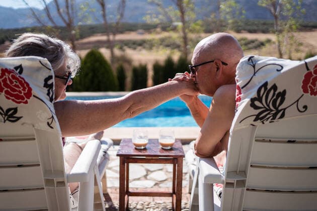 Back view of shirtless loving old husband kissing hand of wife while enjoying summer day on loungers on poolside, Model released JuanAlbertoRuiz_SeniorCoupleSwimmingPool_14.jpg Copyright: xJuanxAlbertoxRuizx MR
