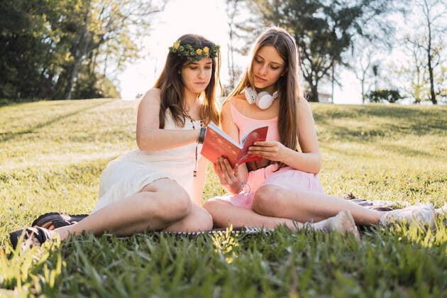 Girlfriends in sundresses sharing textbook while sitting on meadow in sunny park in back lit, Model released ReneStevens_TeenagerFriends_19.jpg Copyright: xRenexStevensx MR
