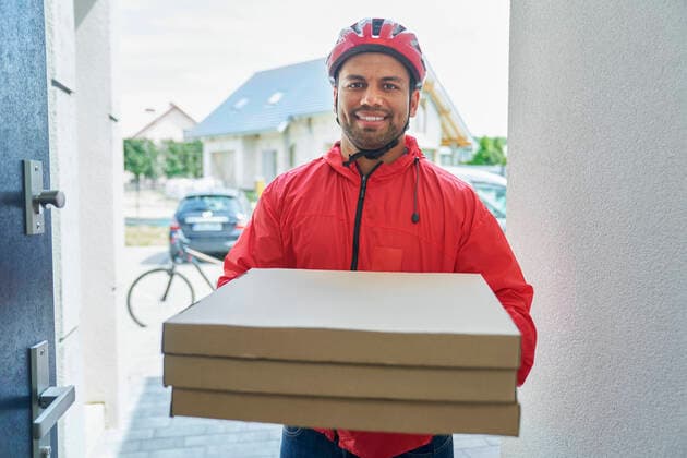 Male delivery person holding pizza box while standing at doorway model released Symbolfoto property released ABIF01453