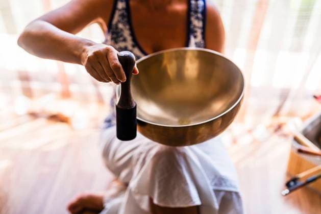 Female sound therapist playing brass bowl with mallet in studio model released Symbolfoto property released DLTSF02130