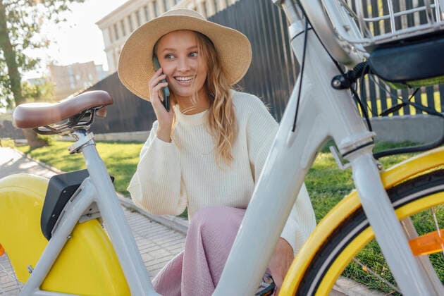 IMAGO Creative: Klimawandel - Zukunft und Innovation Smiling blond woman talking on smart phone while crouching by bicycle model released Symbolfoto VPIF04854