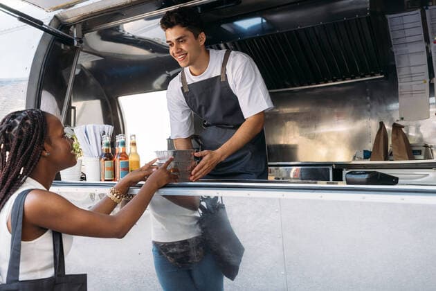 Smiling salesman giving takeaway packaged food to a female customer. Woman taking food from a food truck owner. Copyright: xxArtemxVarnitsinx