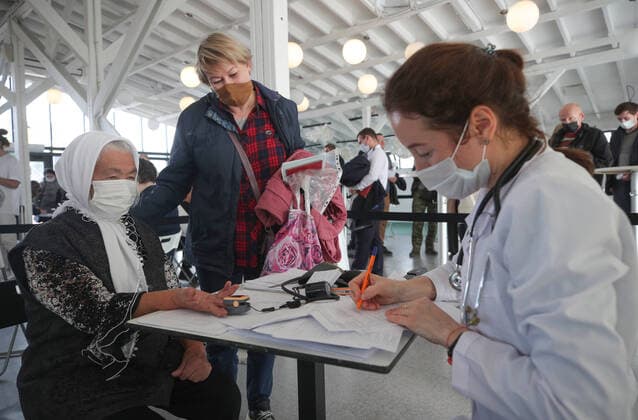 KAZAN, RUSSIA â€” OCTOBER 11, 2021: An elderly woman has paperwork filled in by a medical worker before receiving a vaccine against COVID-19 at a temporary vaccination site outside the Mega shopping centre. Since the start of the pandemic, Tatarstan has confirmed more than 27,000 cases of COVID-19. Since 1 October, the number of new confirmed cases has been increasing in Tatarstan by more than 60 daily. Tatarstan has announced additional restrictions which are coming into force starting from 11 October 2021 in connection with the rising daily number of new COVID-19 cases. People over 65 who havenâ€™t had COVID-19 or havenâ€™t received a vaccine against COVID-19 in the last six months are required to self-isolate. Theatres, cinemas, circuses and c  TS113BEC