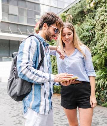 Female in casual clothes and man with backpack standing and looking at screen of smartphone with smile in university yard, Model released AlbertMorcillo_Hairdressing_83.jpg Copyright: xAlbertxMorcillox MR