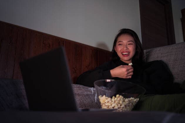 IMAGO Creative: Jahreszeit Winter, Couching Young cheerful Asian female wearing casual clothes sitting on couch and eating popcorn at home watching movie on laptop JuanAlbertoRuiz_Popcorn_8.jpg Copyright: xJuanxAlbertoxRuizx Model Released