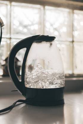 IMAGO Creative: Haushaltsger?te - Wasserkocher Transparent electric kettle with black handle and lid and with boiling water placed on white table in kitchen LosMuertosCrew_Ageing_44.jpg Copyright: xLosxMuertosxCrewx Model Released
