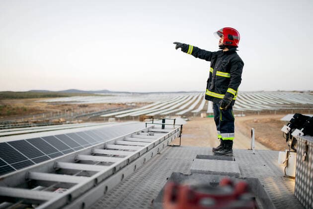 IMAGO Creative: Landleben, Mit Nachhaltigkeit gr?n auf dem Land leben Full body side view of male firefighter wearing uniform and gloves standing on metal roof of fire engine near ladder with hand pointing forward at solar panels in rural farm, Model released SergioVictorVega_Firefighter_16.jpg Copyright: xSergioxVictorxVegax MR