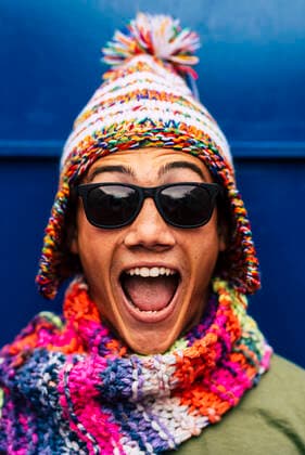 Happy male teenager with multi colored knit hat and scarf in front of blue wall model released Symbolfoto SIPF02458