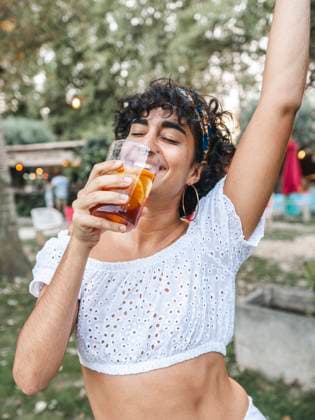 IMAGO Creative: Sommer, Sommertage im Garten Positive ethnic female drinking refreshing cocktail and dancing while enjoying party in summer garden, Model released AlbertMorcillo_Finalsummer_28.jpg Copyright: xAlbertxMorcillox MR