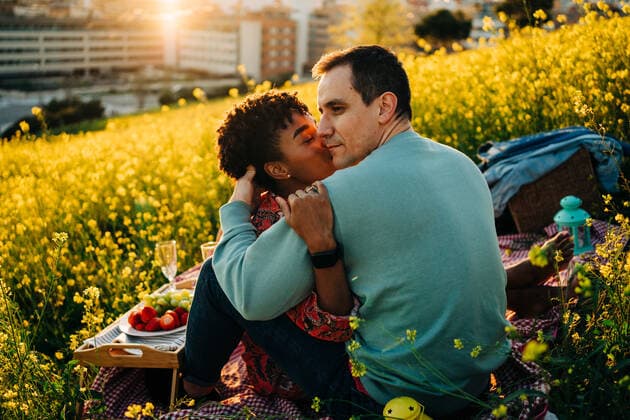Young African American lady with curly hair embracing and kissing cheek of romantic boyfriend with closed eyes during picnic on blooming meadow on sunny day, Model released JakeJakab_EliAndSergio_7.jpg Copyright: xJakexJakabx MR