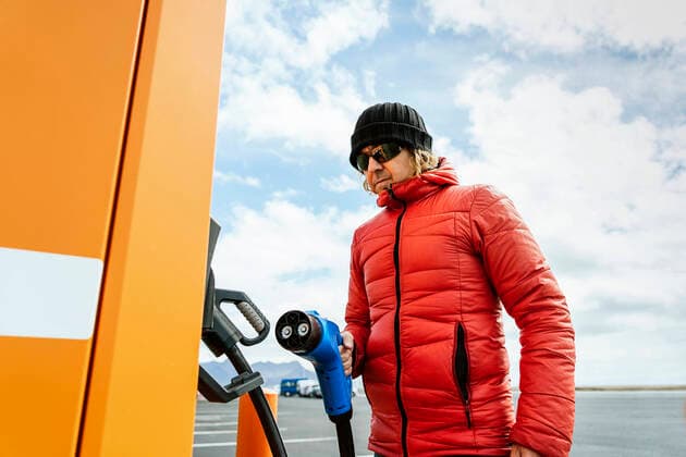 IMAGO Creative: Corporate: Klimaschutz, Digitalisierung und Urbanisierung From below of thoughtful male in warm outwear and hat standing with charging power to electric vehicle in hand at gas station in sunny day JavierBallester_IcelandJune_36.jpg Copyright: xJavierxBallesterx Model Released