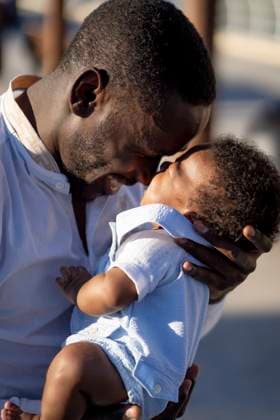 Side view of careful African American father in shirt standing and embracing little baby with curly hair on street in sunny day, Model released OscarCarrascosa_AfricanFamily_13.jpg Copyright: xOscarxCarrascosax MR