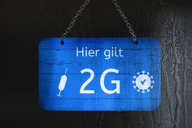 Germany, Bavaria - 29 October 2021: Sign with inscription Hier gilt 2G Regel, 2G rule symbol image in front of rainy window pane - unvaccinated people must stay outside