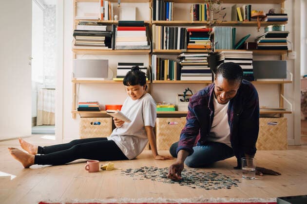 Man playing jigsaw puzzle while girlfriend reading book in living room Sweden, Stockholm, model released, property released Copyright: xMaskotx , MA90008