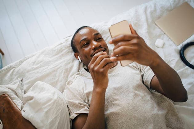 Smiling mid adult man using mobile phone while lying on bed Sweden, Stockholm, model released, property released Copyright: xMaskotx , MA90076