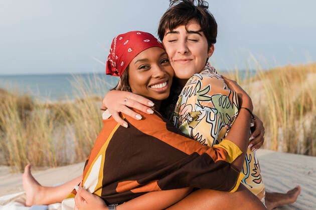 Smiling lesbian women embracing at beach model released, JRVF02042