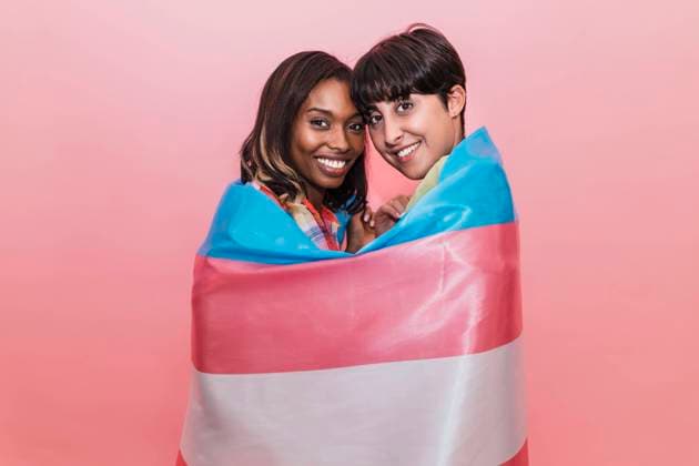 IMAGO Creative: Internationaler Tag der Sichtbarkeit von Transgender am 31. März Smiling girlfriends covered in transgender flag by pink background model released, JRVF02074